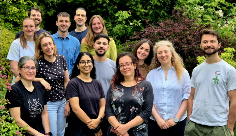 Members of the Briscoe lab standing together outdoors in a garden, with trees and shrubs behind them